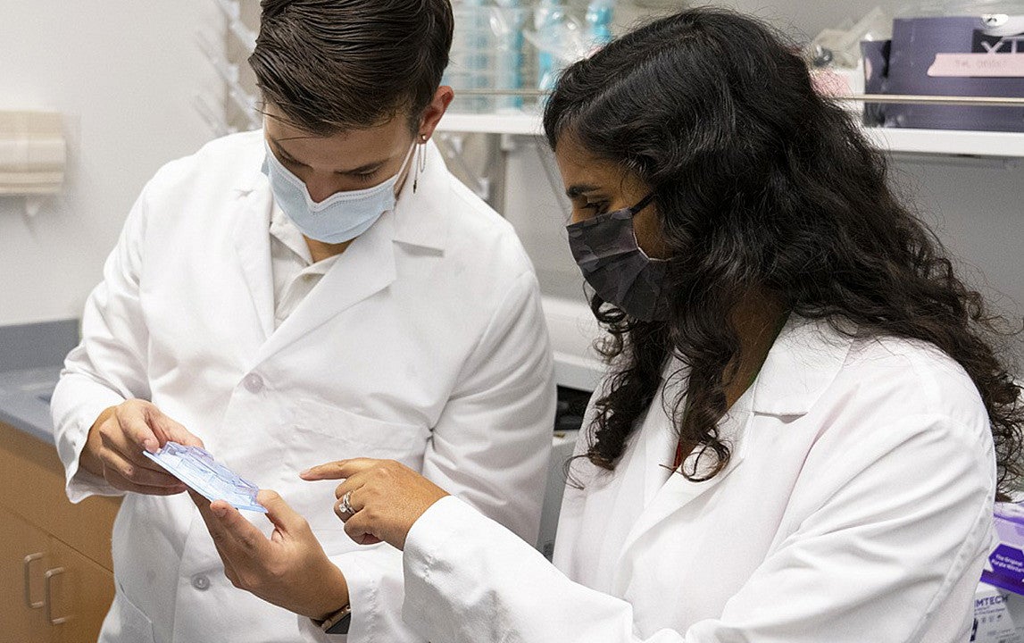 A man and woman in white lab coats look at a medical device