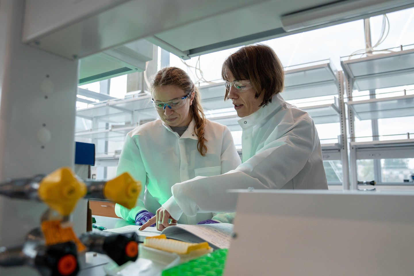 Two people wearing white coats and safety goggles in a lab