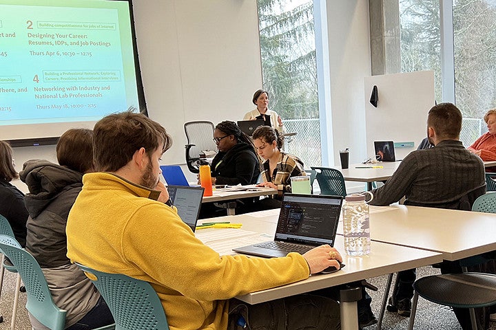 A group of people sit at tables in a classroom