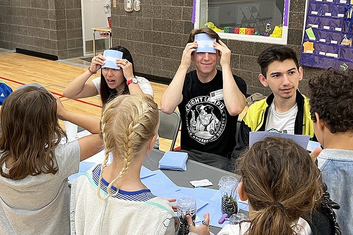 Three adults demonstrate heat transfer paper to kids