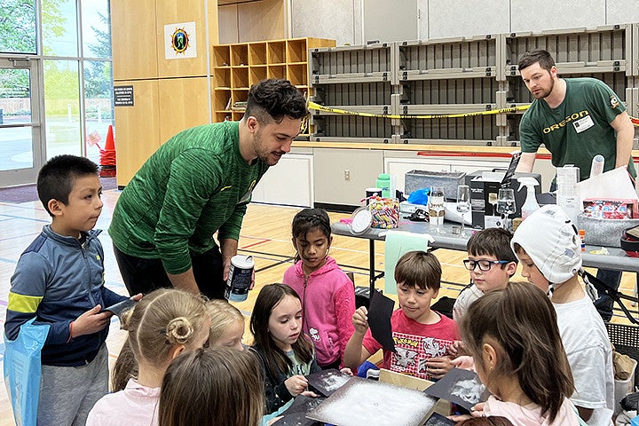 Two adults explain sound vibrations to a group of kids