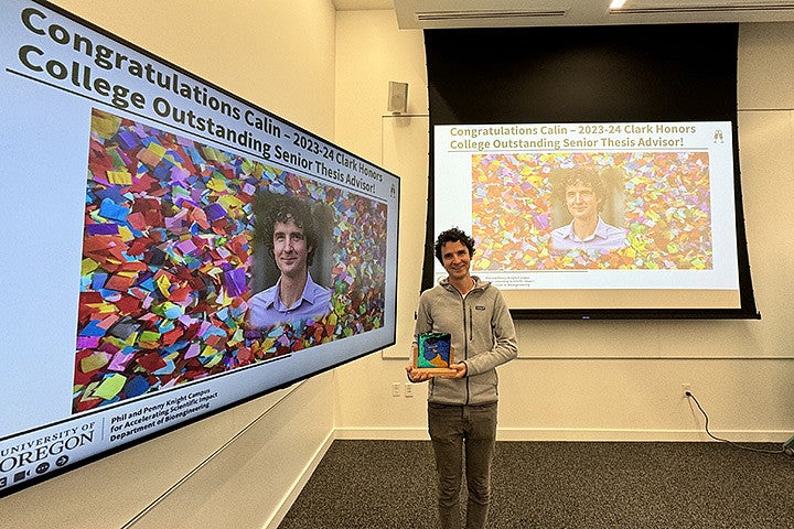 A man holds an award next to two large screens with his photo