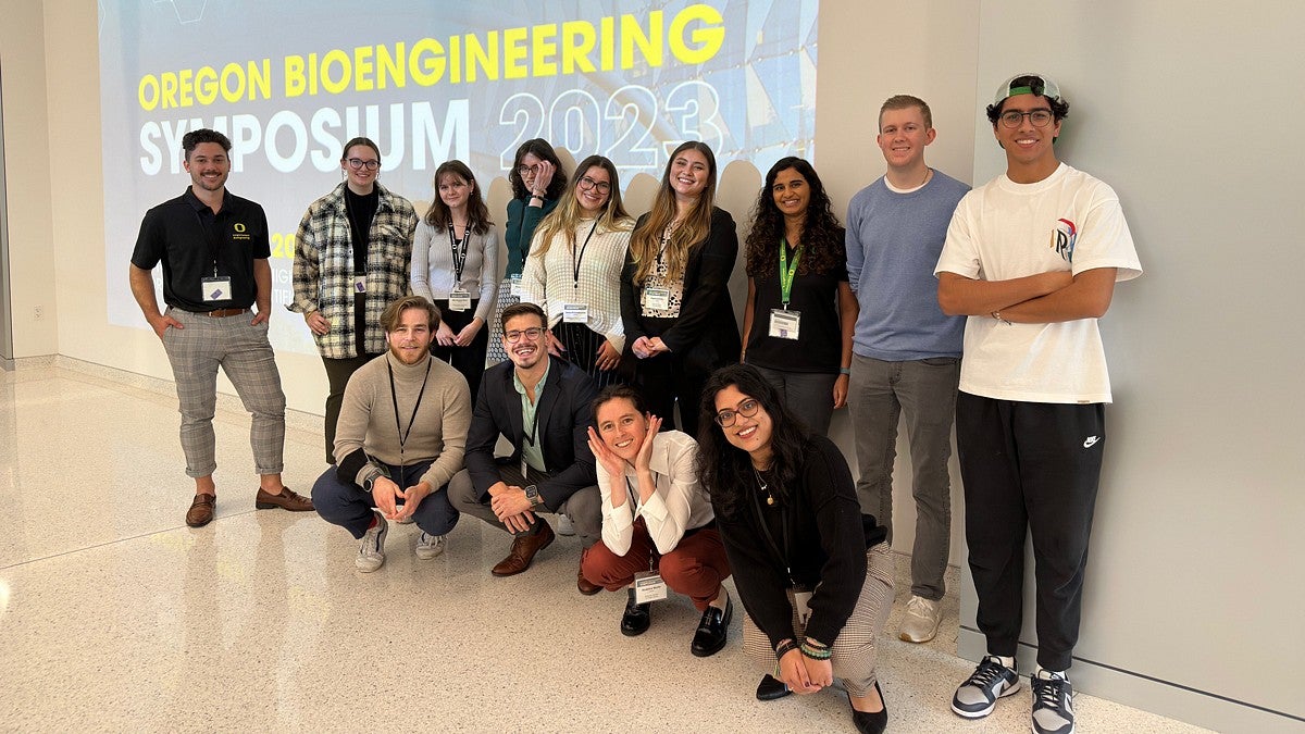 Group of attendees at the Oregon Bioengineering Symposium 2023 posing for a photo in front of a banner displaying the event's title.