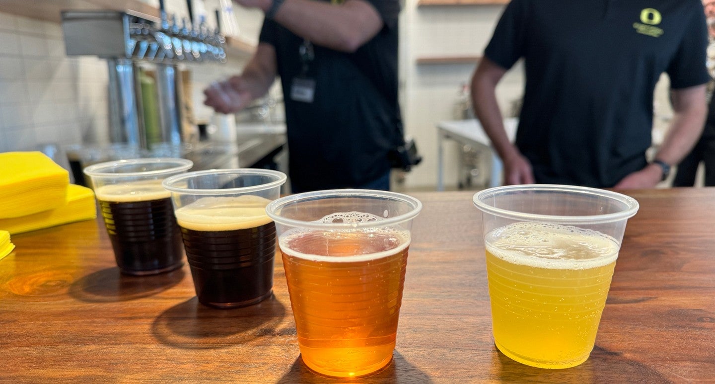 four cups of beer with two people in background