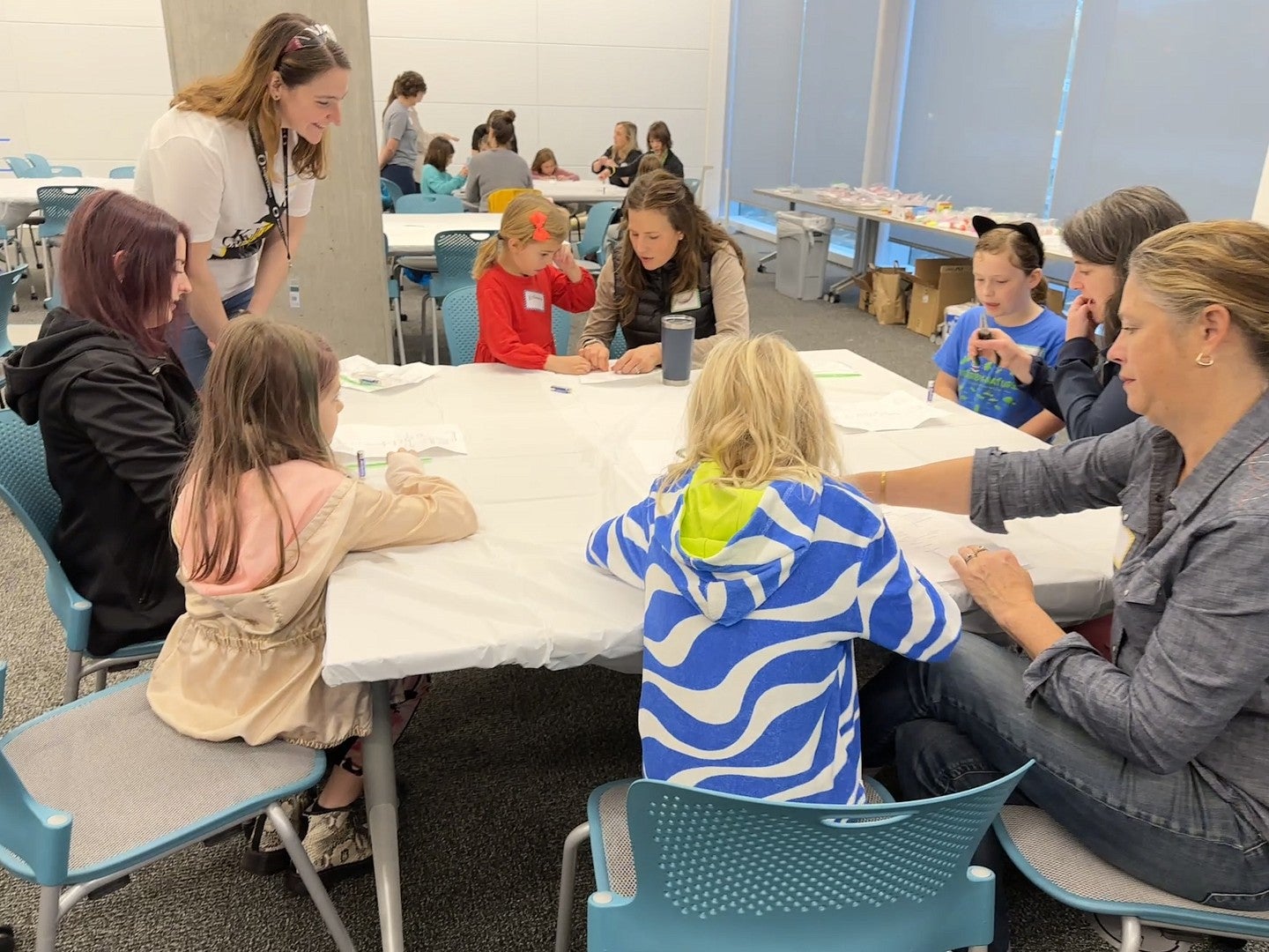 Multiple people gathered around a table with art supplies, some engaged in projects