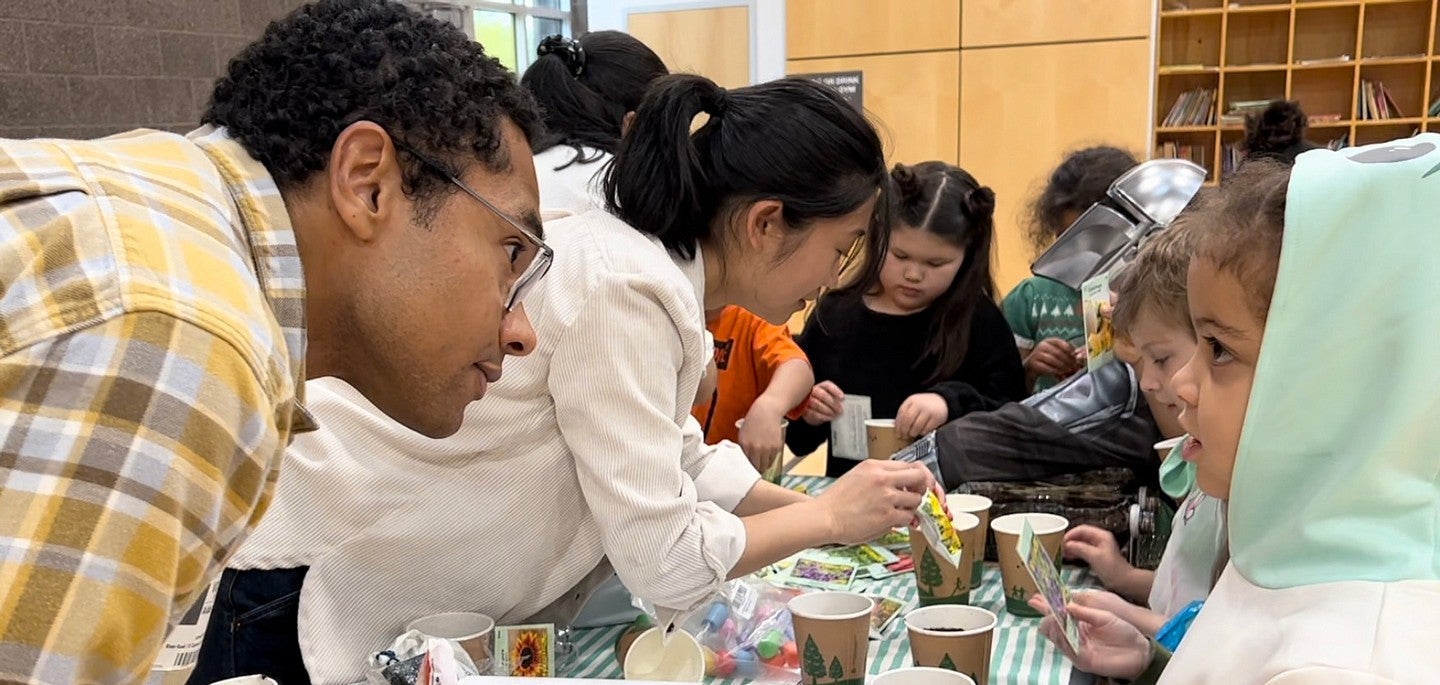 Instructor on left looks to student on right, instructor in center background helps students with science experiments