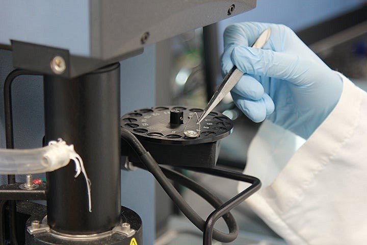 A close up of a hand in a blue latex glove holding tweezers on a machine