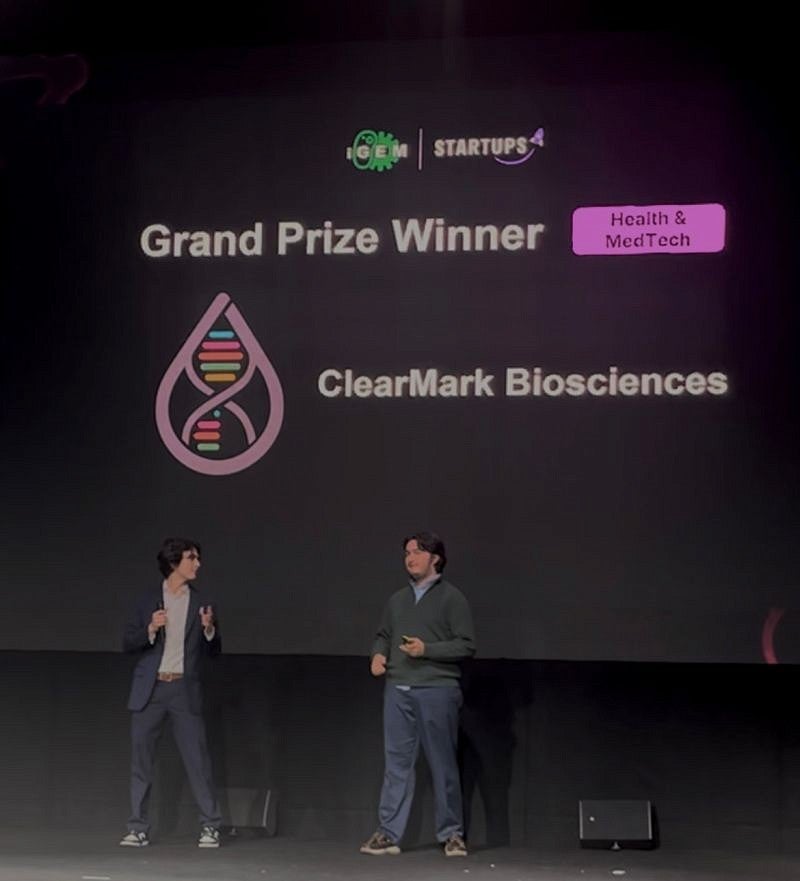 Two people on stage before a backdrop that reads "iGEM startups" and "Grand Prize Winner"