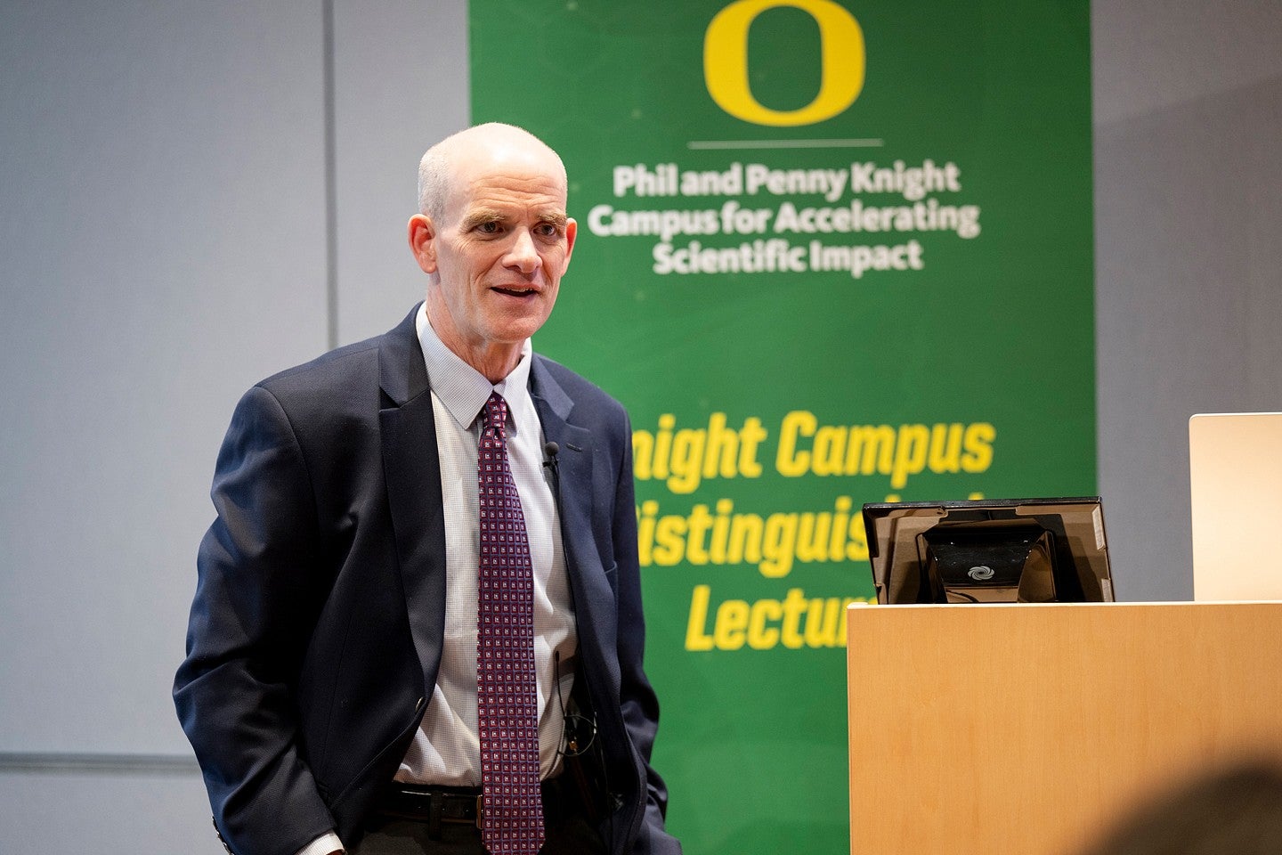 Picture of man before a backdrop that reads Phil and Penny Knight Campus for Accelerating Scientific Impact and "Distinguished Lecture Series"