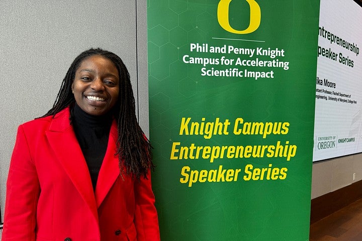 Erika Moore stands to the left of a sign with the words Phil and Penny Knight Campus for Accelerating Scientific Impact