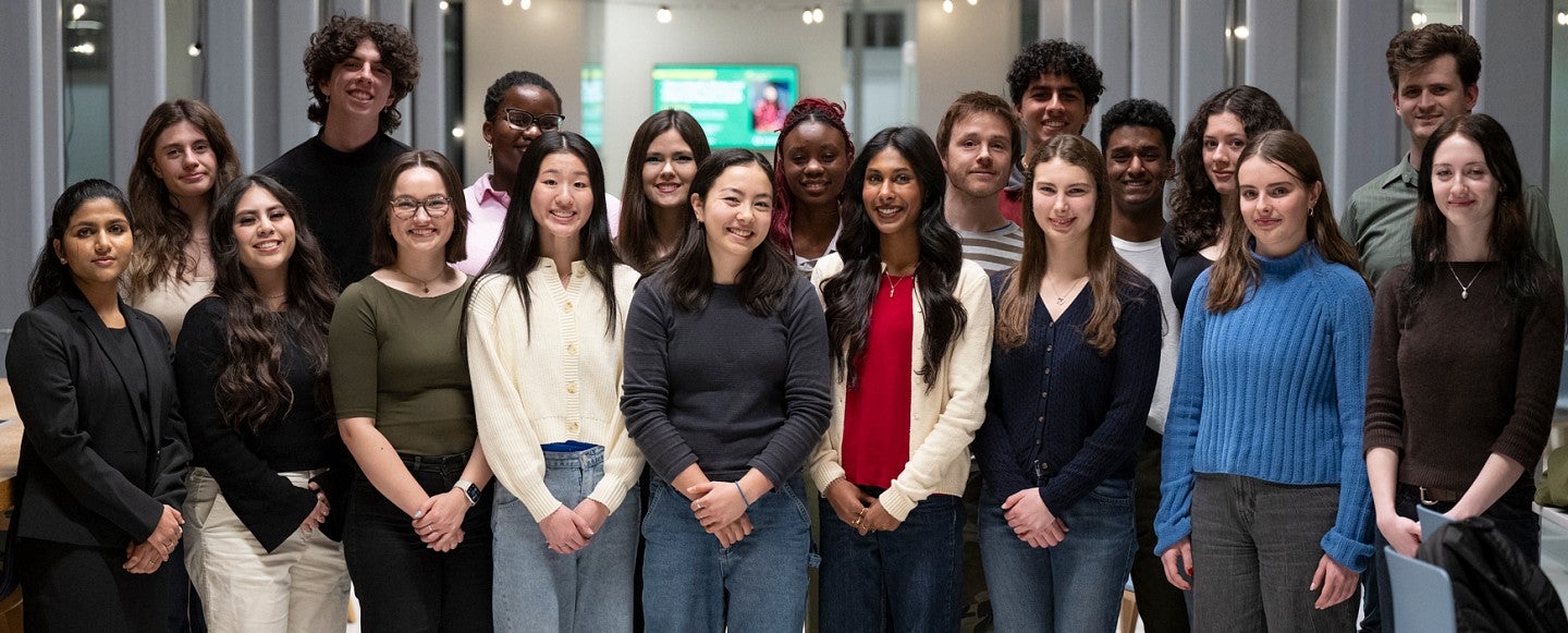 Group of students in glass hallway looking directly toward camera with legs cropped off