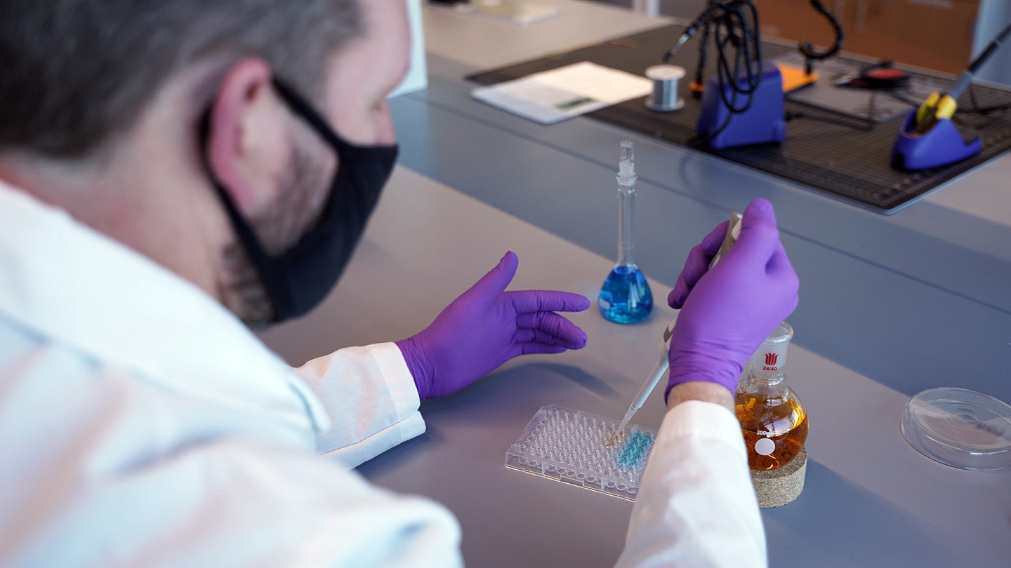 a person pipetting colored liquid into a clear well plate