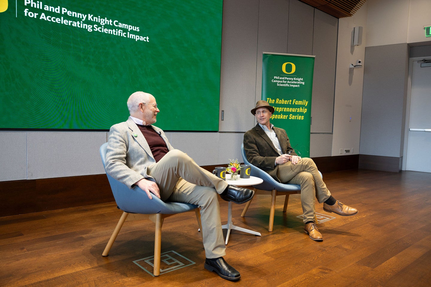 Michael Weickert and Bob Guldberg sitting in chairs in front of a screen during the Winter 2026 Robert Family Entrepreneurship Speaker Series