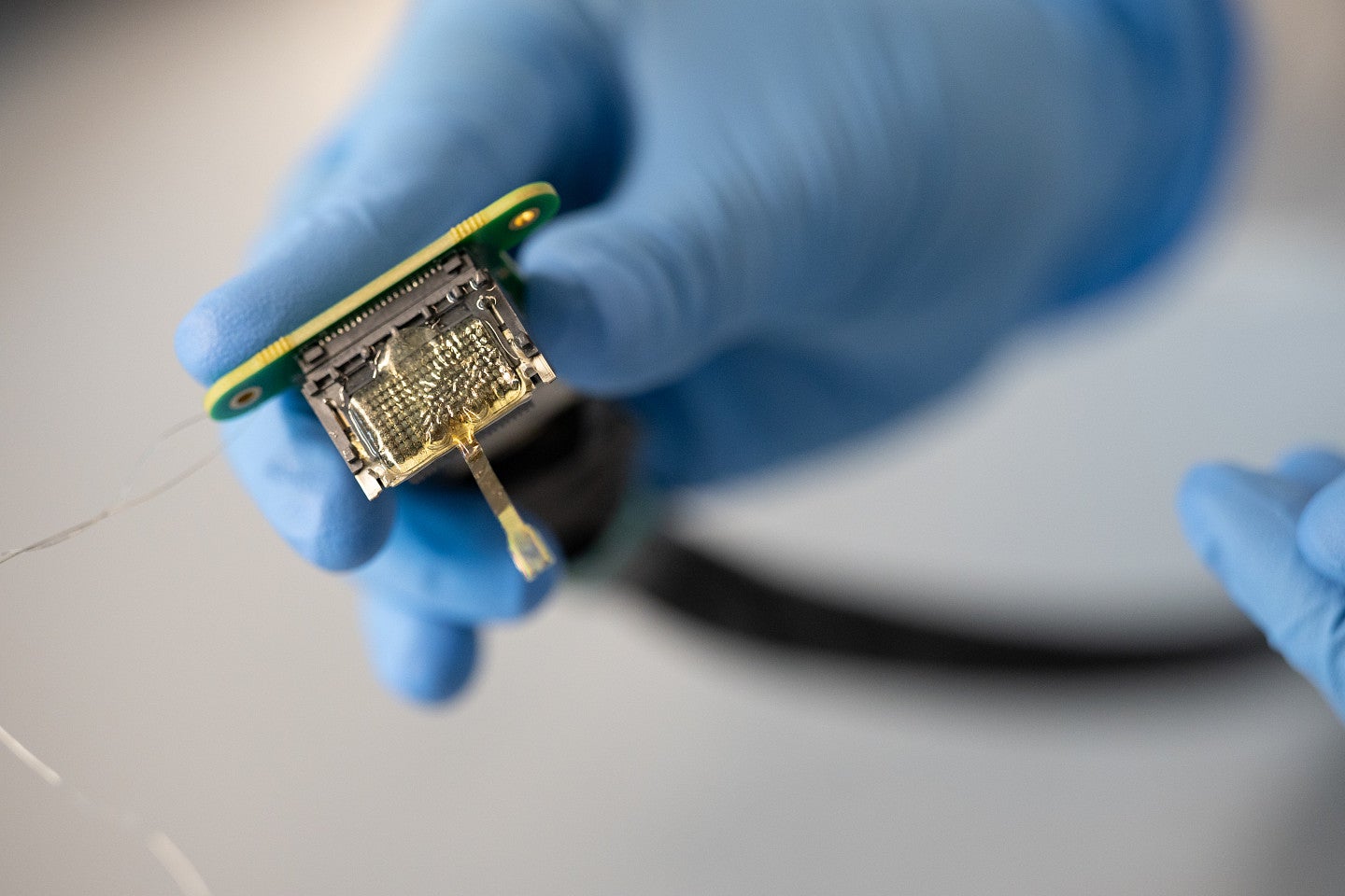 a thin array electrode, shown with electrical boards and someone holding with a blue glove, in the Deku lab at the Knight Campus