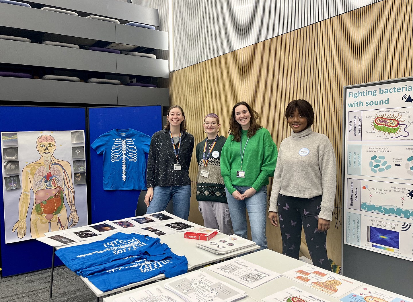 Sara Keller with other scientists in front of a table with some images of skeletons and the human body