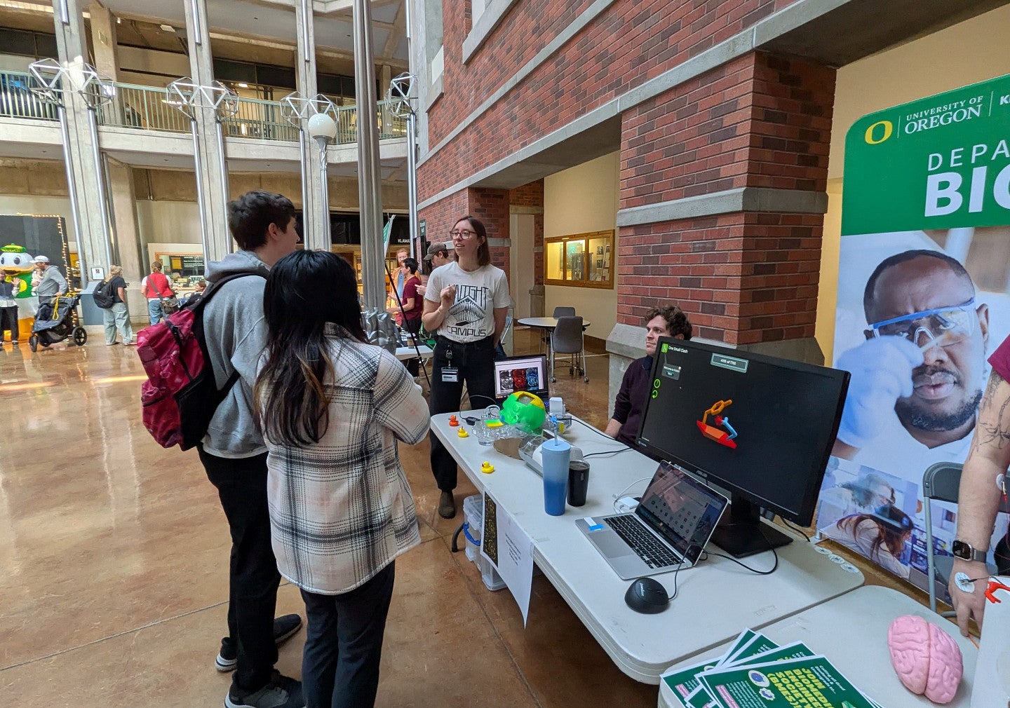 Sara Keller talking to some students, in front of a table, by a brick wall, speaking about bioengineering