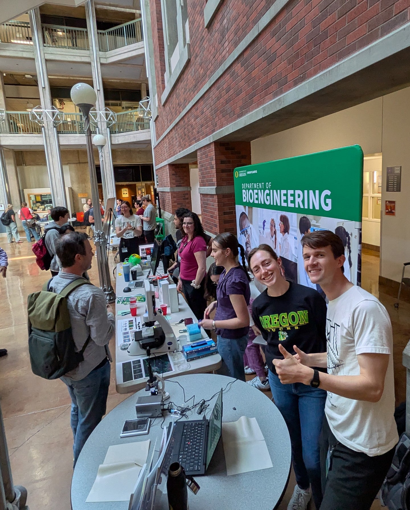 David and Taylor talking to students, in an atrium with brick and signage for Bioengineering in the background