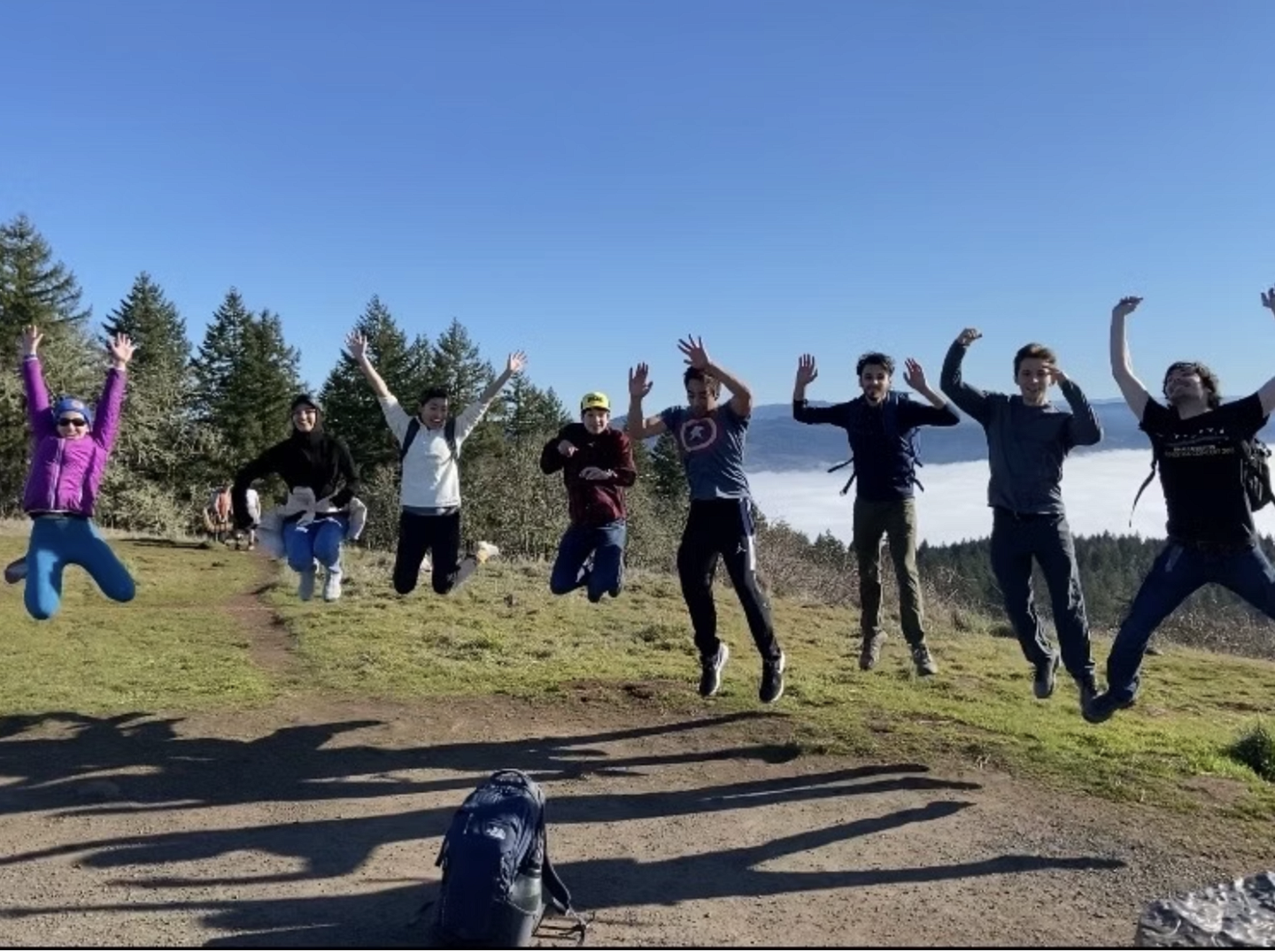 group of people jumping with their arms up, on top of Mt. pisgah - with trees and clouds in the background