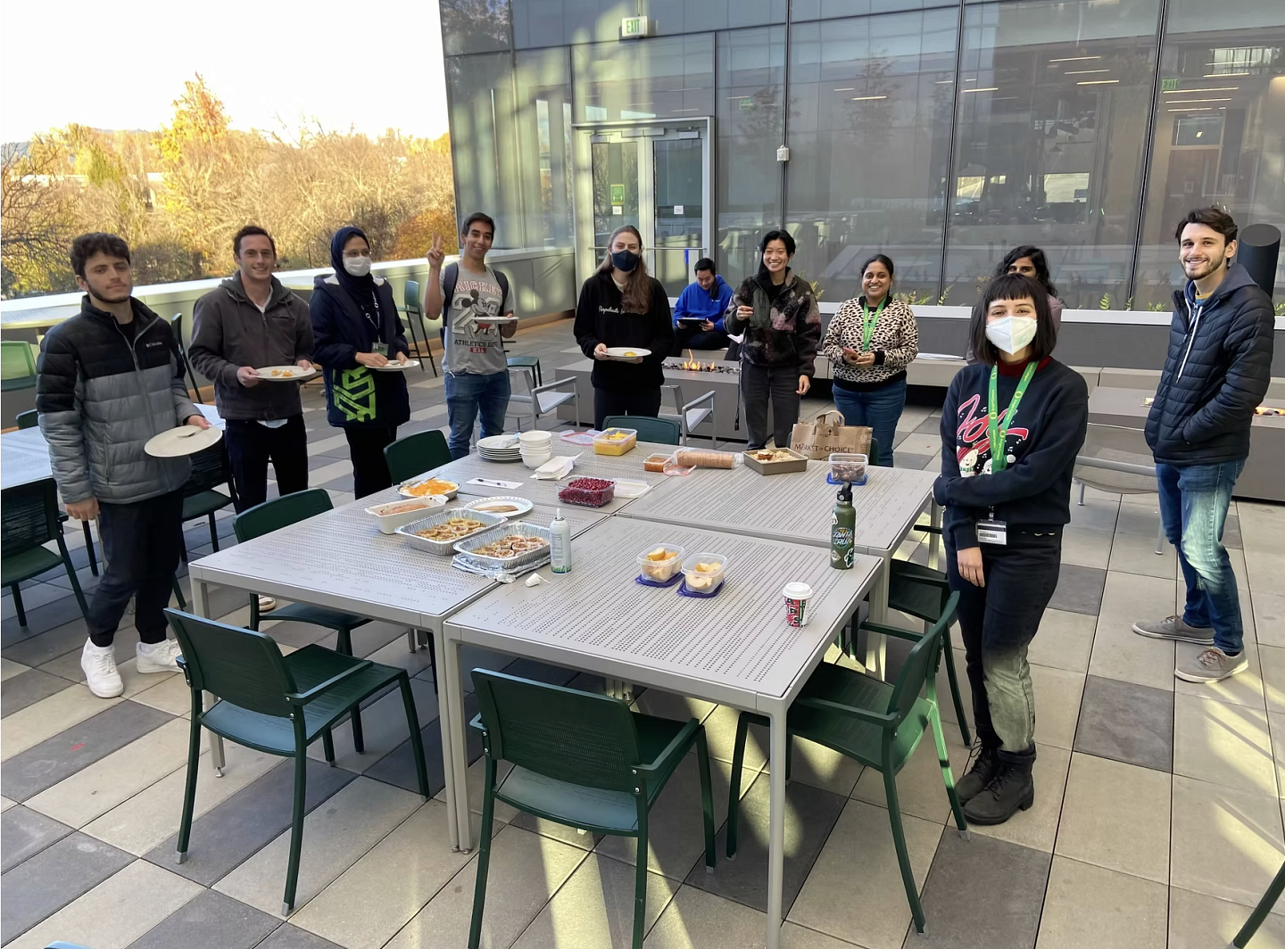 A group of people standing around the table, which has a variety of baked goods.