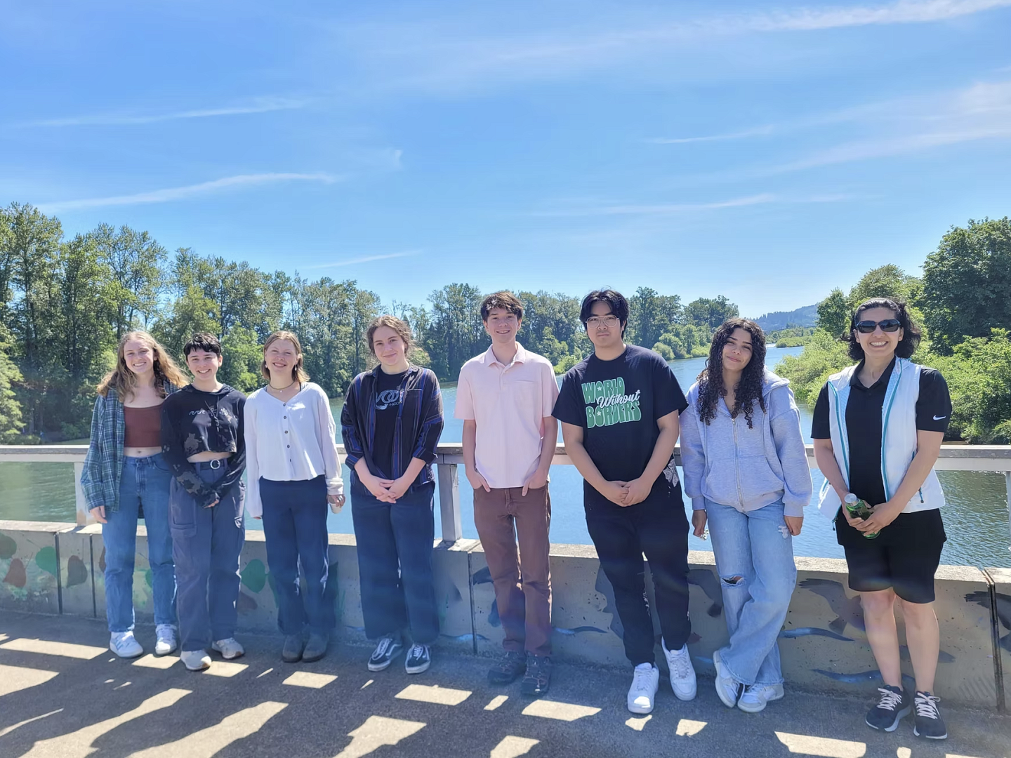 a group of people on a bridge, overlooking the blue willamette river on a sunny day