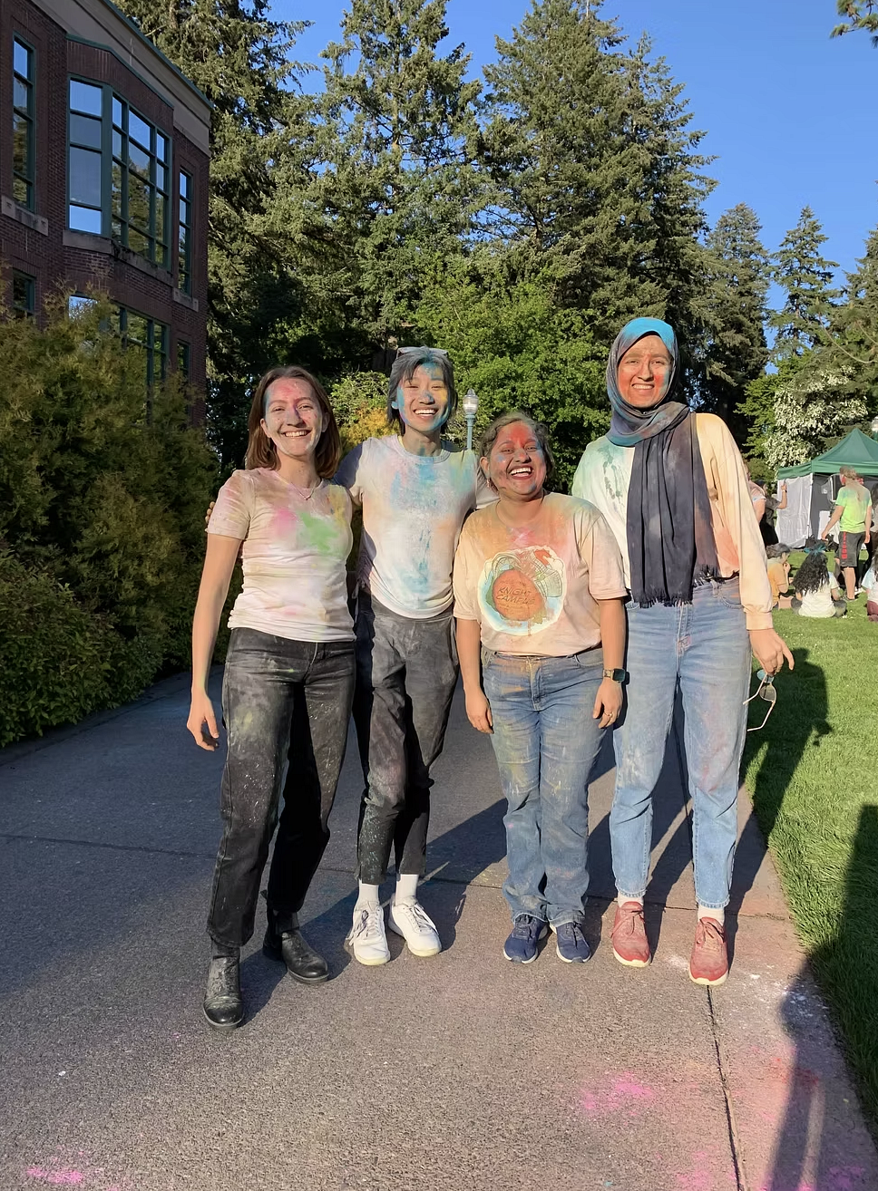 group of students smiling, looking at the camera, wearing white shirts with colored powder over them for a Holi celebration