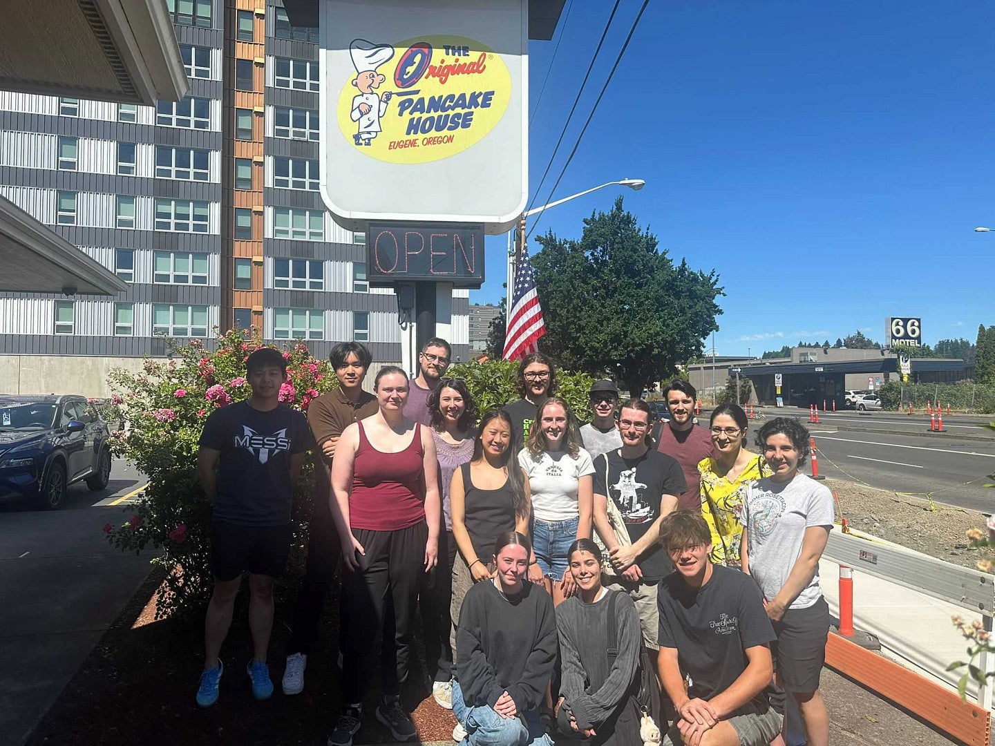 A group of people outside, in front of the 'original pancake house' sign, with blue skies and next to a road