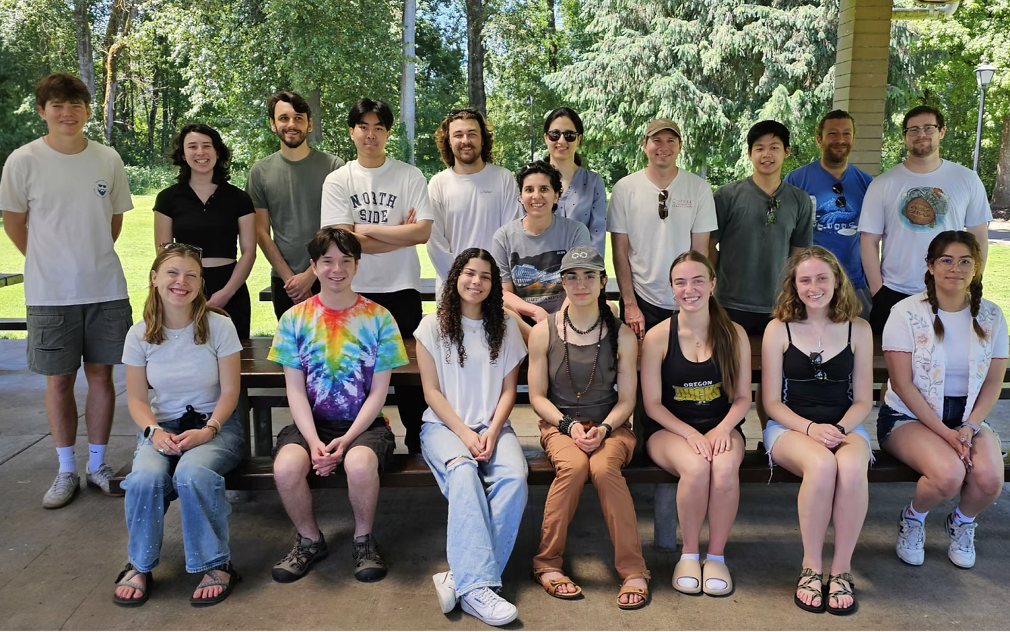 A large group of people, all lined up or seated, in a park on a sunny day, looking at the camera and smiling
