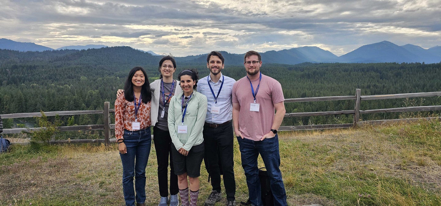 A group of people in front of a mountain scene, with a rugged wooden fence
