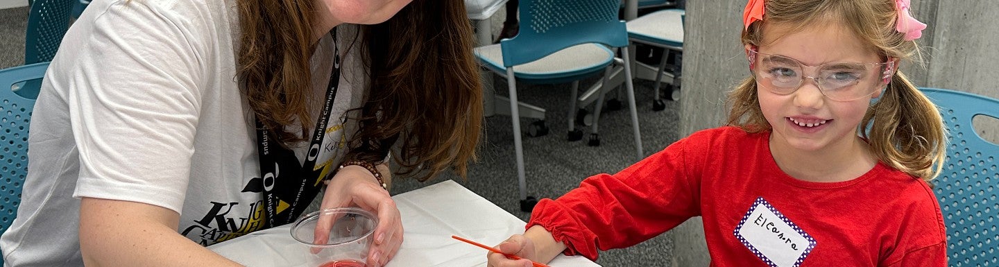 Adult and child painting together at a table during a workshop, with other participants in the background.