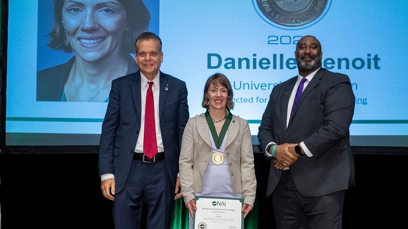 Presentation of an award to Danielle Benoit at a 2024 event of the National Academy of Engineering, featuring three individuals on stage with a large projection screen 