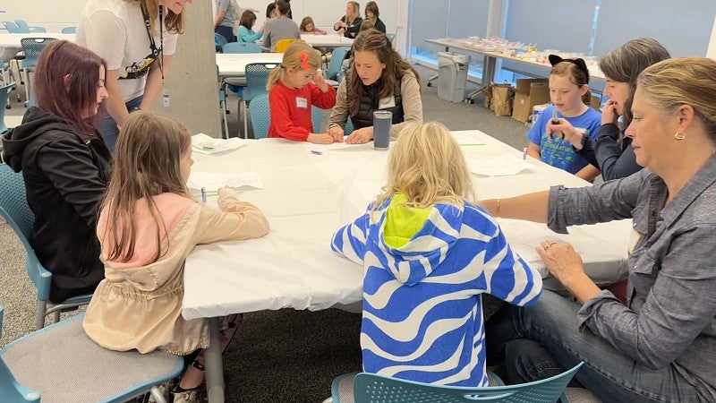 Multiple people gathered around a table with art supplies, some engaged in projects