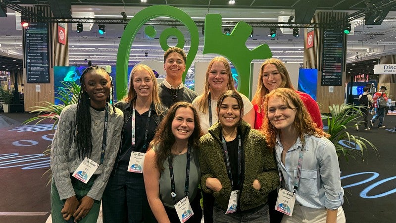 Knight Campus-based iGEM team standing before green iGEM logo statue in a conference hall