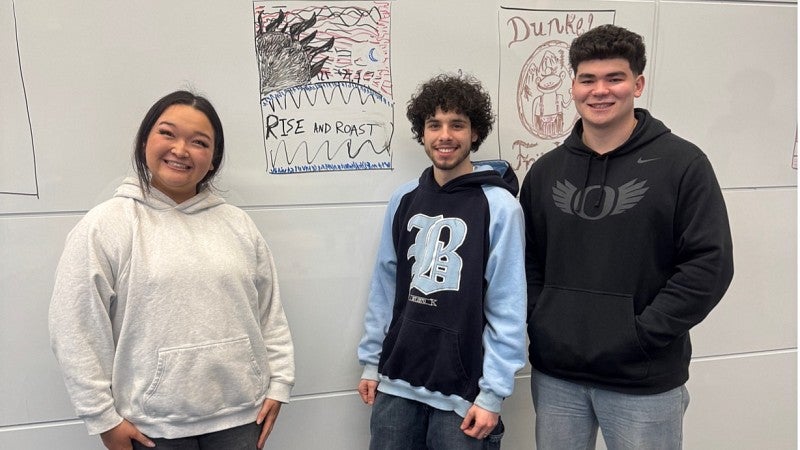 Three peopel standing in front of white board with illustration