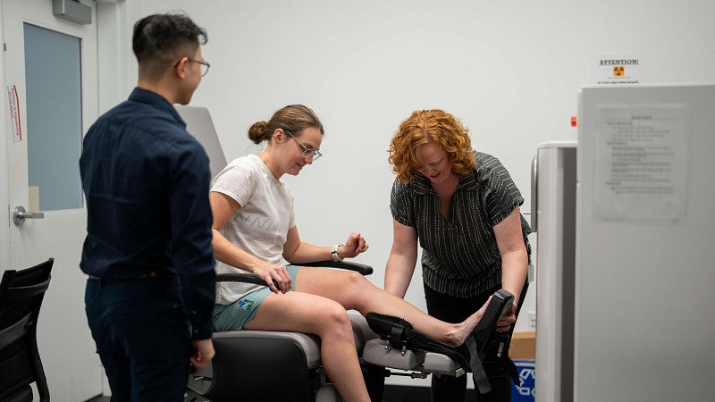 A woman getting her leg scanned in a machine, assisted by two other people