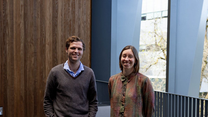 Two people standing outside on a terrace, with wood wall features behind them