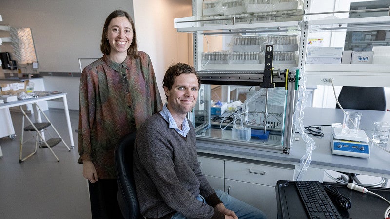 Two people standing at a computer, with some electronic equipment