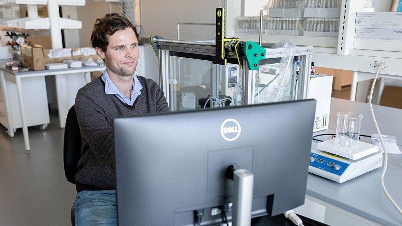 A man looking at a monitor with lab, and ultrasound equipment, behind him