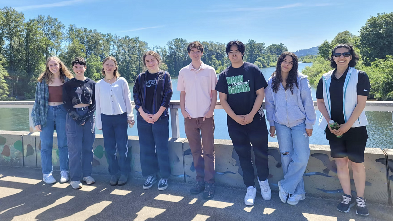 a group of people on a bridge, overlooking the blue willamette river on a sunny day