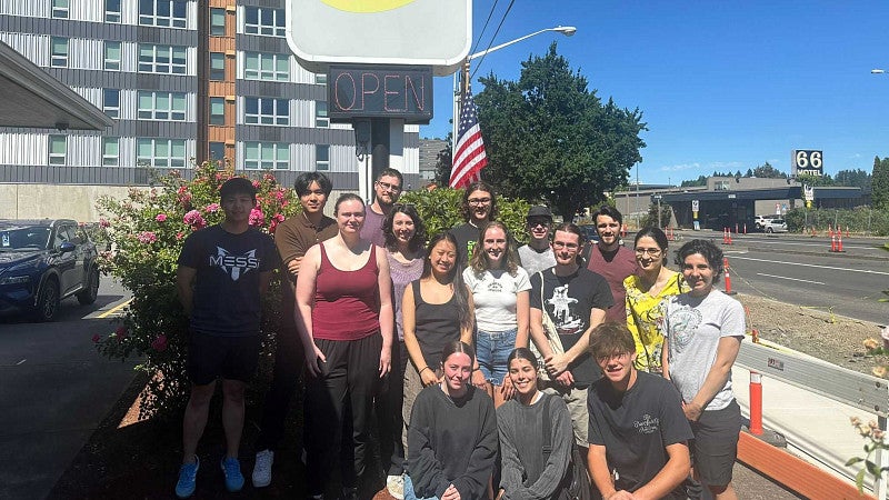 A group of people outside, in front of the 'original pancake house' sign, with blue skies and next to a road
