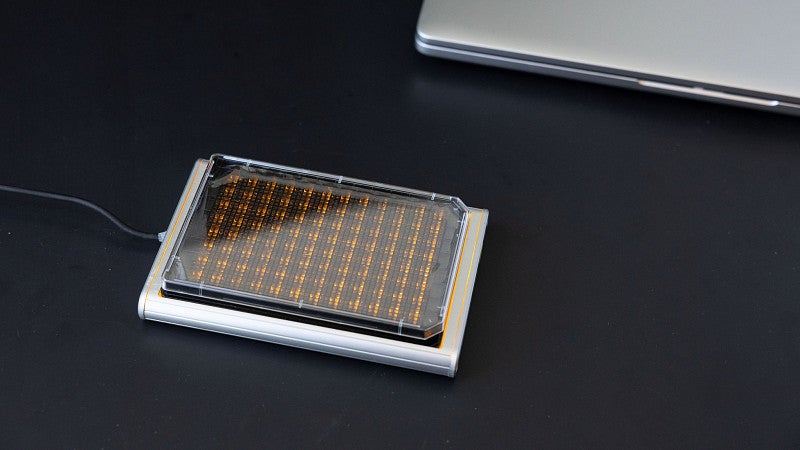 a 96 well plate that looks orange, is covered, and connected to a computer