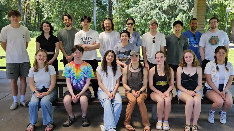 A large group of people, all lined up or seated, in a park on a sunny day, looking at the camera and smiling