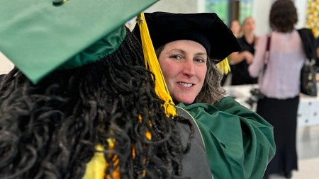 Person hugging graduate with green cap in foreground