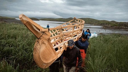 People carrying canoe frame through tall grass