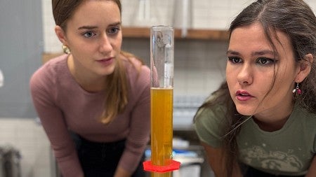 Two people looking intently at a graduated cylinder with liquid