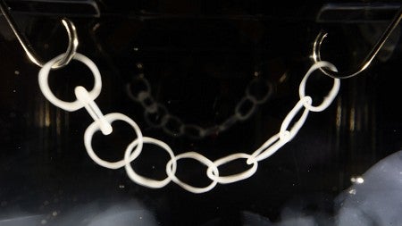 a 3D chain link printed with VAM - black background with a tan, gelly like chain