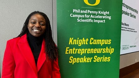 Erika Moore stands to the left of a sign with the words Phil and Penny Knight Campus for Accelerating Scientific Impact