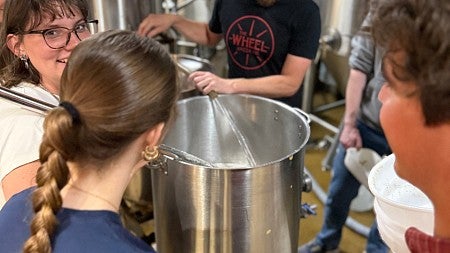 Students stand around a pot in a brewery learning how to make beer