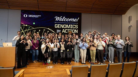 a large group of participants at 2026 genomics in action, in the seminar room, holding the "o"