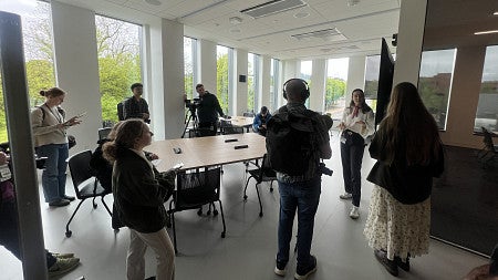 A student talking to a group of reporters in a white classroom with lots of natural light