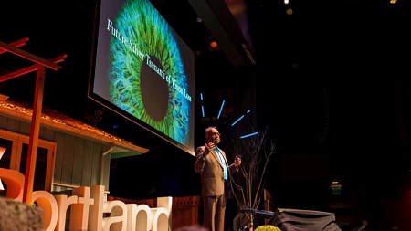 Man on stage with eyeball image on screen behind him